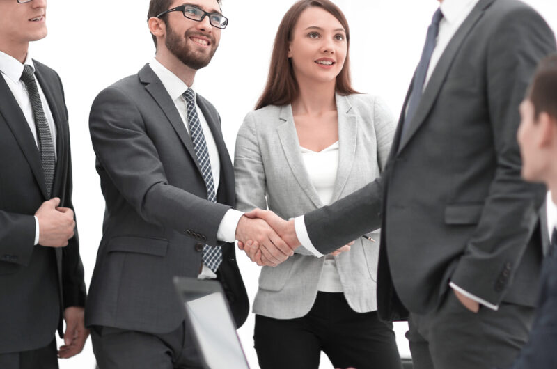 Business colleagues sitting at a table during a meeting with two Business partners handshaking over business objects on workplace.